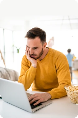 Male in bright yellow long sleeve shirt browsing the web for the perfect loan on a laptop.