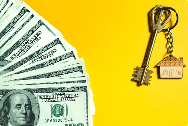 One-hundred-dollar bills sprawled out across a yellow backdrop with a key and a home-shaped wooden keychain to symbolize home equity. 