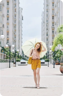 Young woman walking on a large sidewalk with a yellow sun umbrella overtop her head, smiling after unlocking a lower monthly payment.