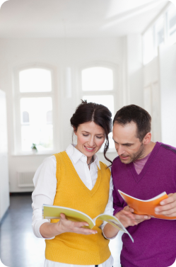 Married couple wearing bright colored sweaters in good spirits as they read brochures about the loan process.